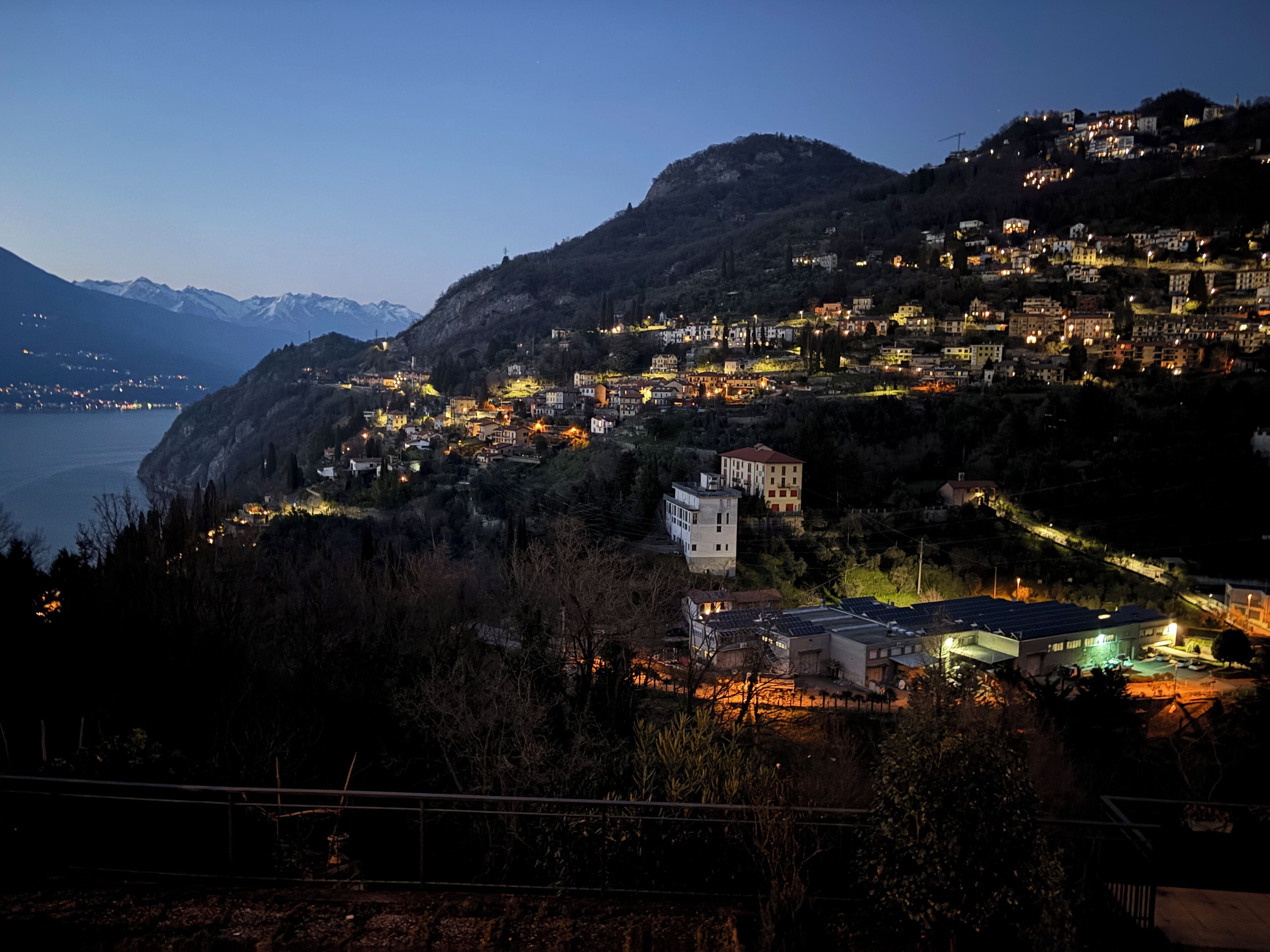 Une ville côtière au crépuscule, avec des bâtiments illuminés se détachant sur un paysage montagneux.