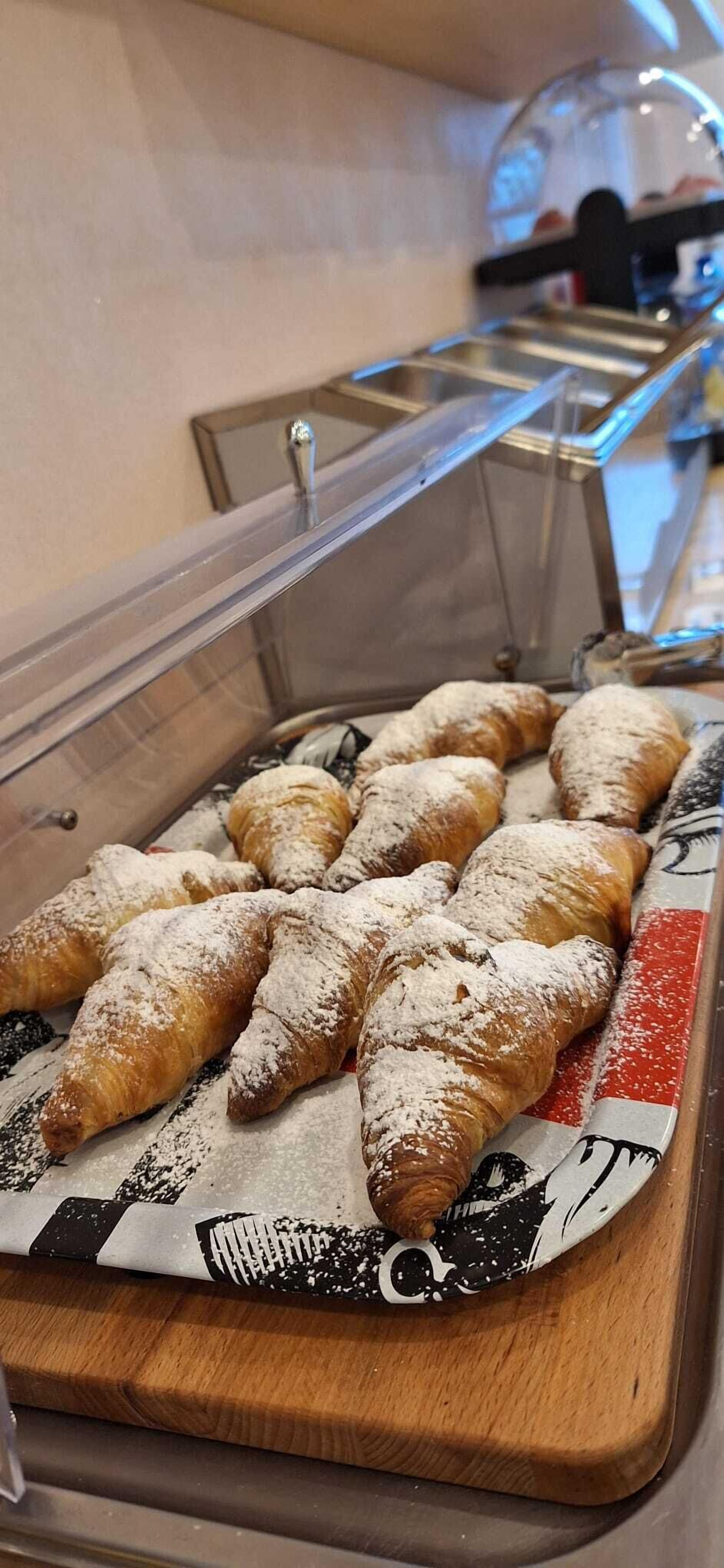 A display case with pastries, including croissants and other baked goods, dusted with powdered sugar.