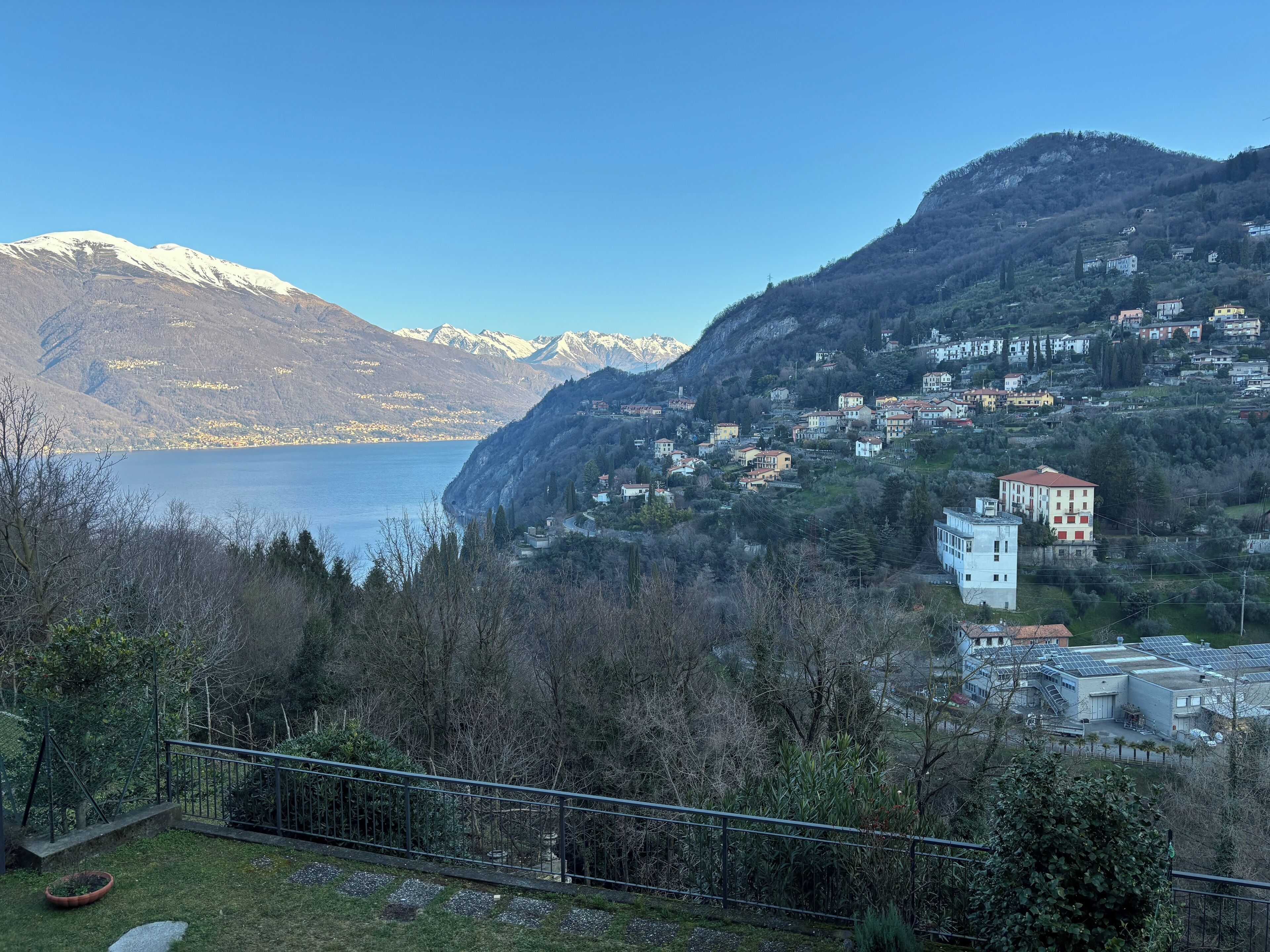 Paisatge montaños amb un llac, cases i un edifici amb panells solars.