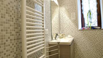 Un baño con pared de azulejos, un lavamanos blanco, un espejo y una ventana con cortina.