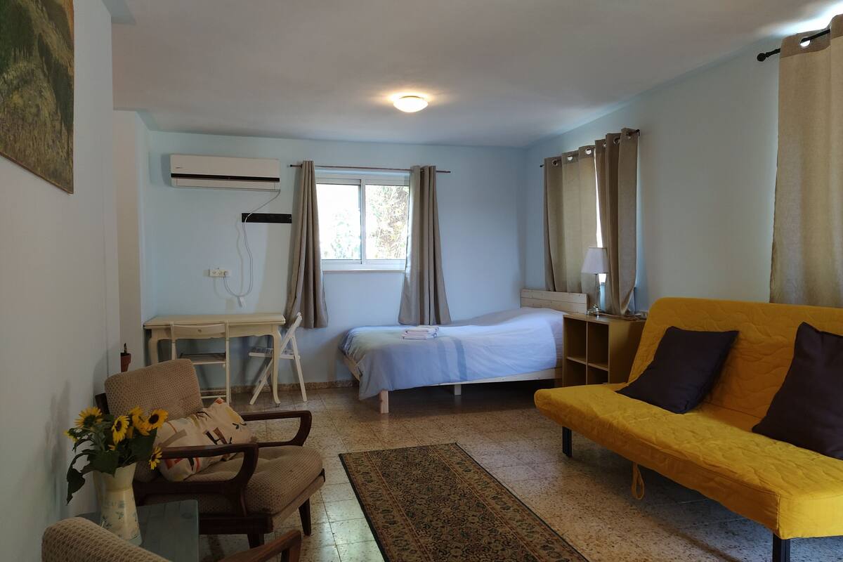 Ein Zimmer mit einem Bett, einem gelben Sofa, einem Schreibtisch und einem Sessel.