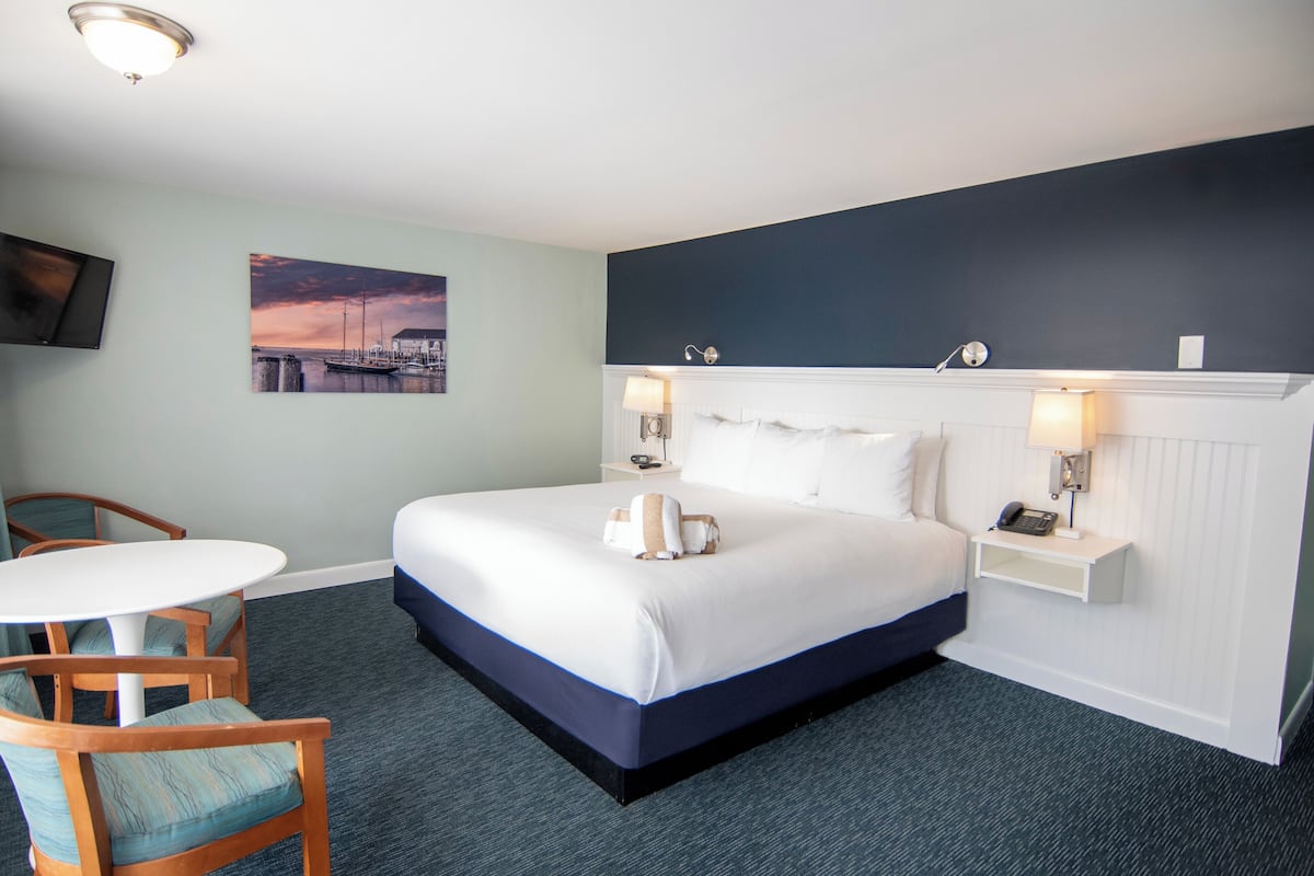 A hotel room with a bed, bedside tables, a chair, a small table, and a painting on the wall.