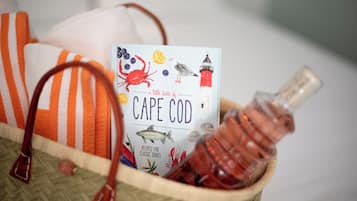 A basket containing a book titled 'Cape Cod', a bottle of liquor, and a striped towel.