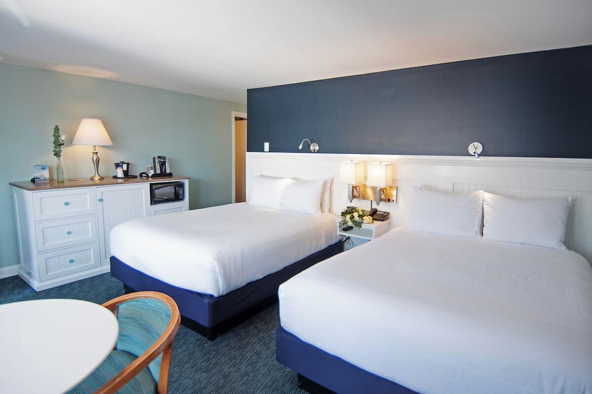 A hotel room with two beds, a desk, a chair, and a small table.