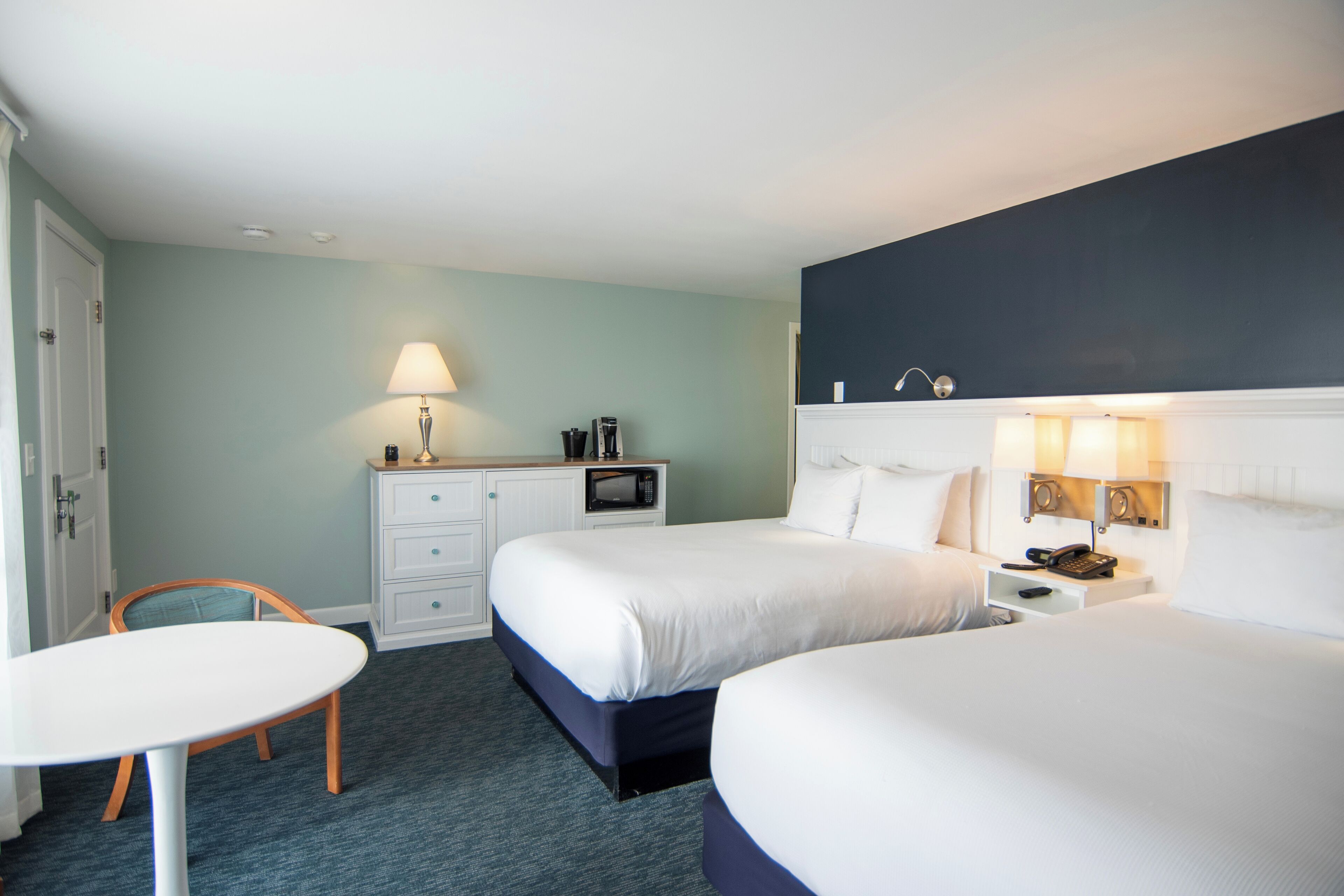 Een hotelkamer met twee bedden, een bureau, een stoel, een lamp en een magnetron.