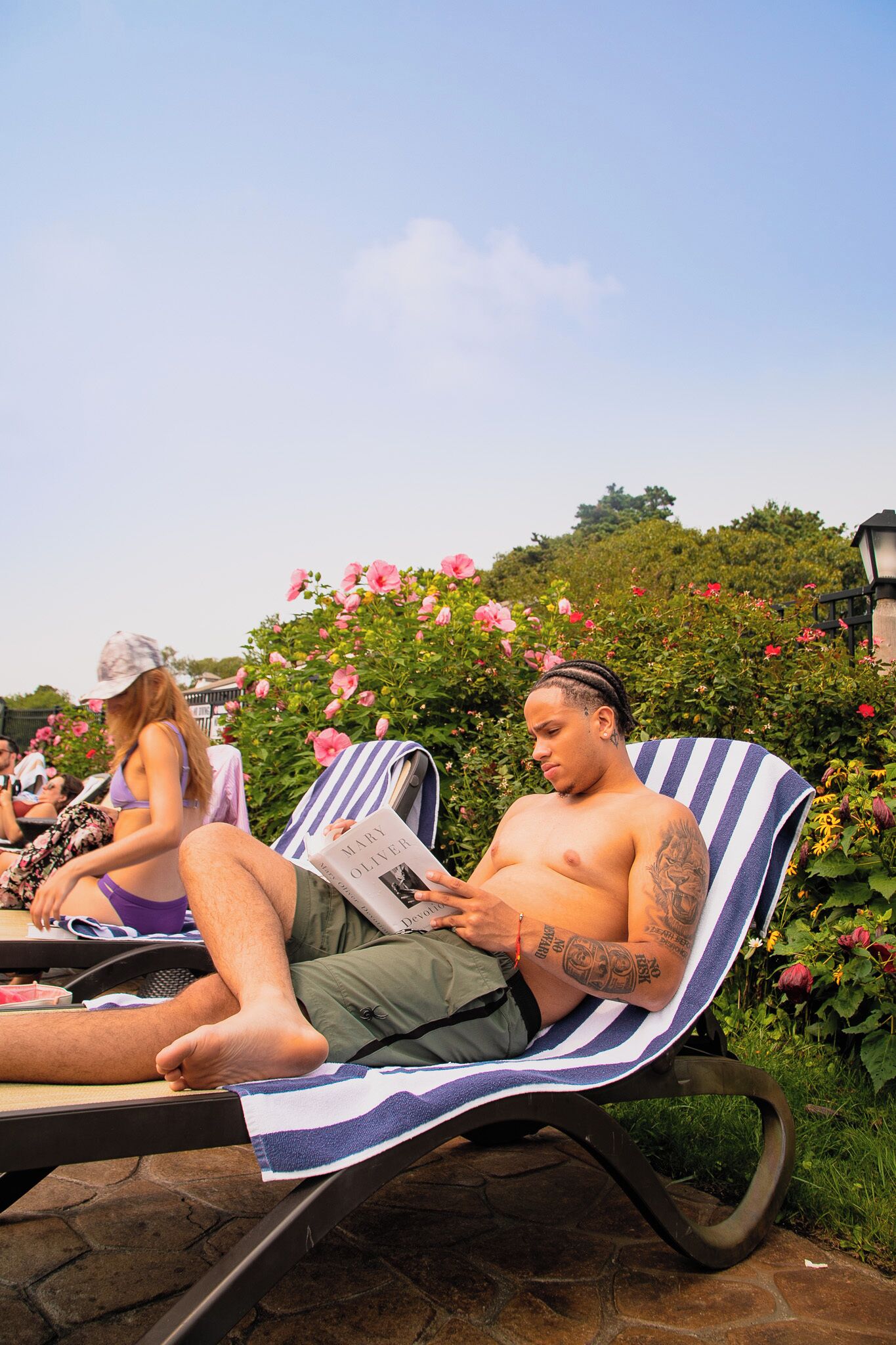 Two people relaxing on striped lounge chairs outdoors with a garden and flowers in the background.