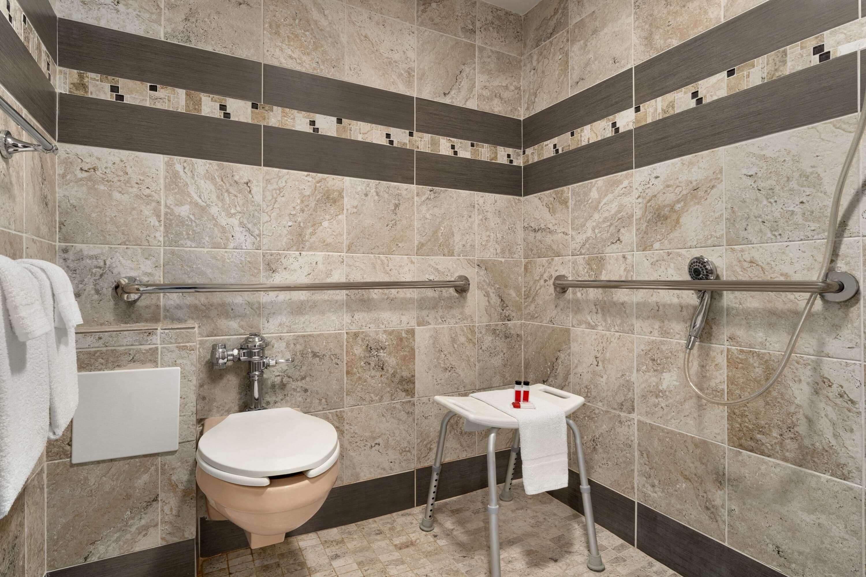 A bathroom with a toilet, sink, and shower. It has grab bars and a towel rack.
