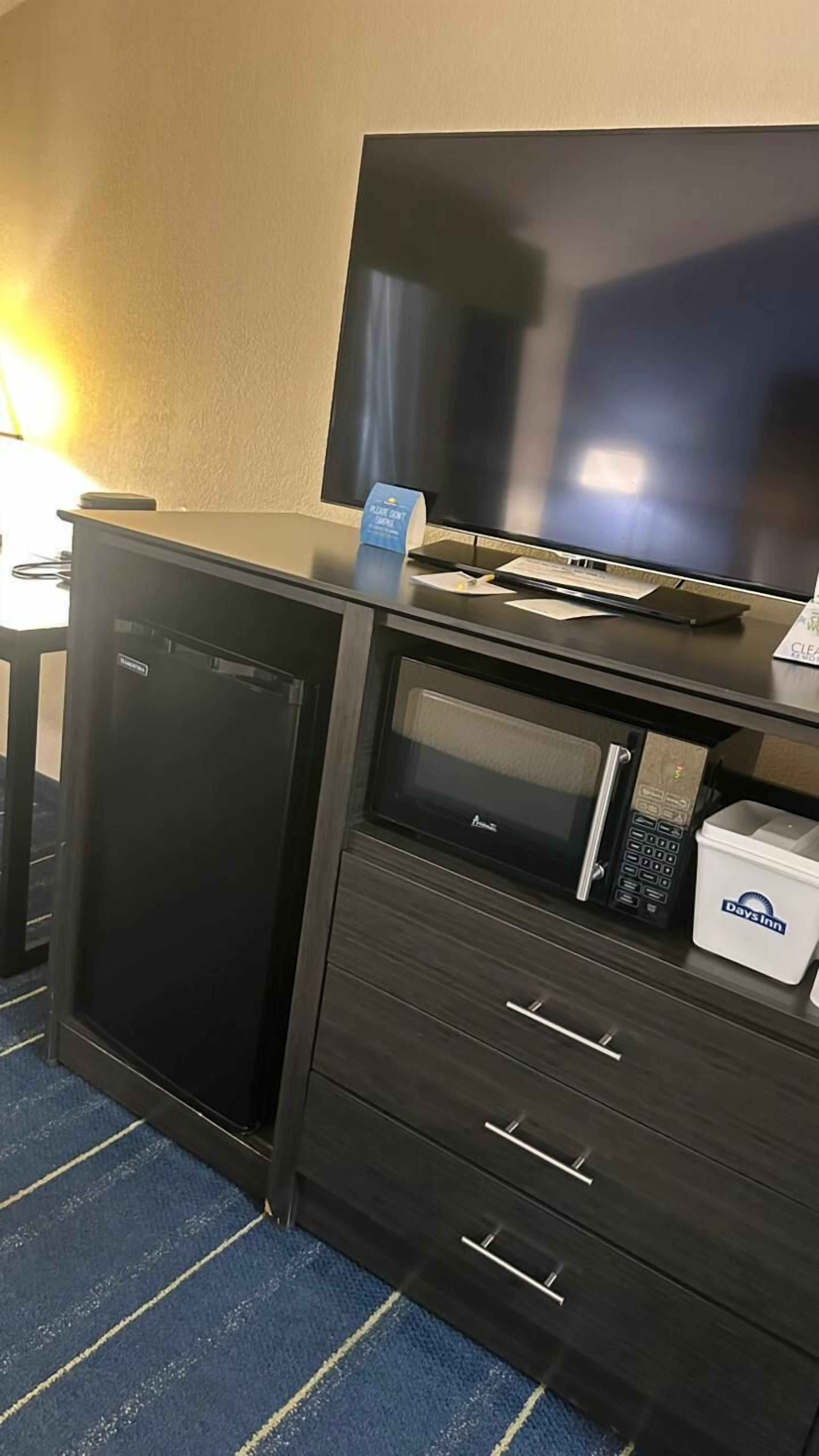 A compact hotel room with a kitchenette, a television, a minibar, and a blue carpet.