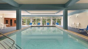 A swimming pool with blue chairs and a view of greenery outside. - Days Inn by Wyndham Tamworth (Chocorua)