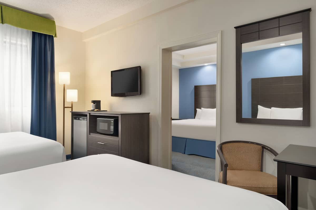 A hotel room with two beds, a desk with a television, a chair, and a mirror.