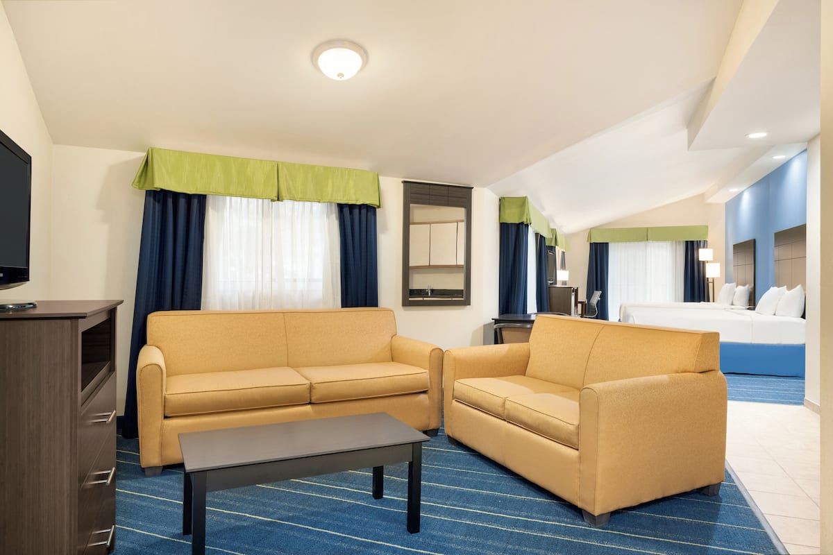 A hotel room with a sofa, a small table, a TV, a bed, and a mirror.