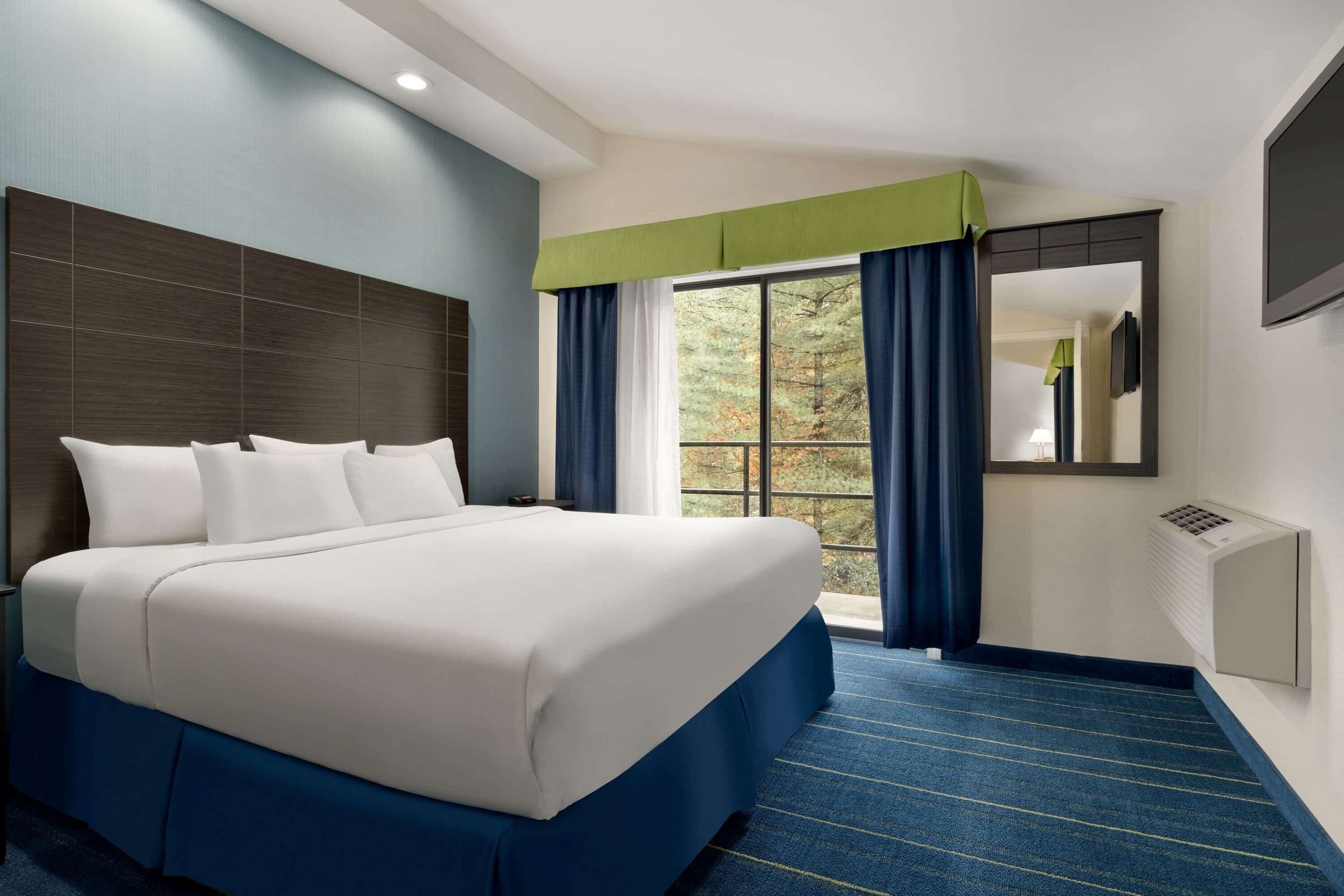 Habitación de hotel con una cama grande, una ventana con cortinas, un televisor de pantalla plana y un aire acondicionado de pared.