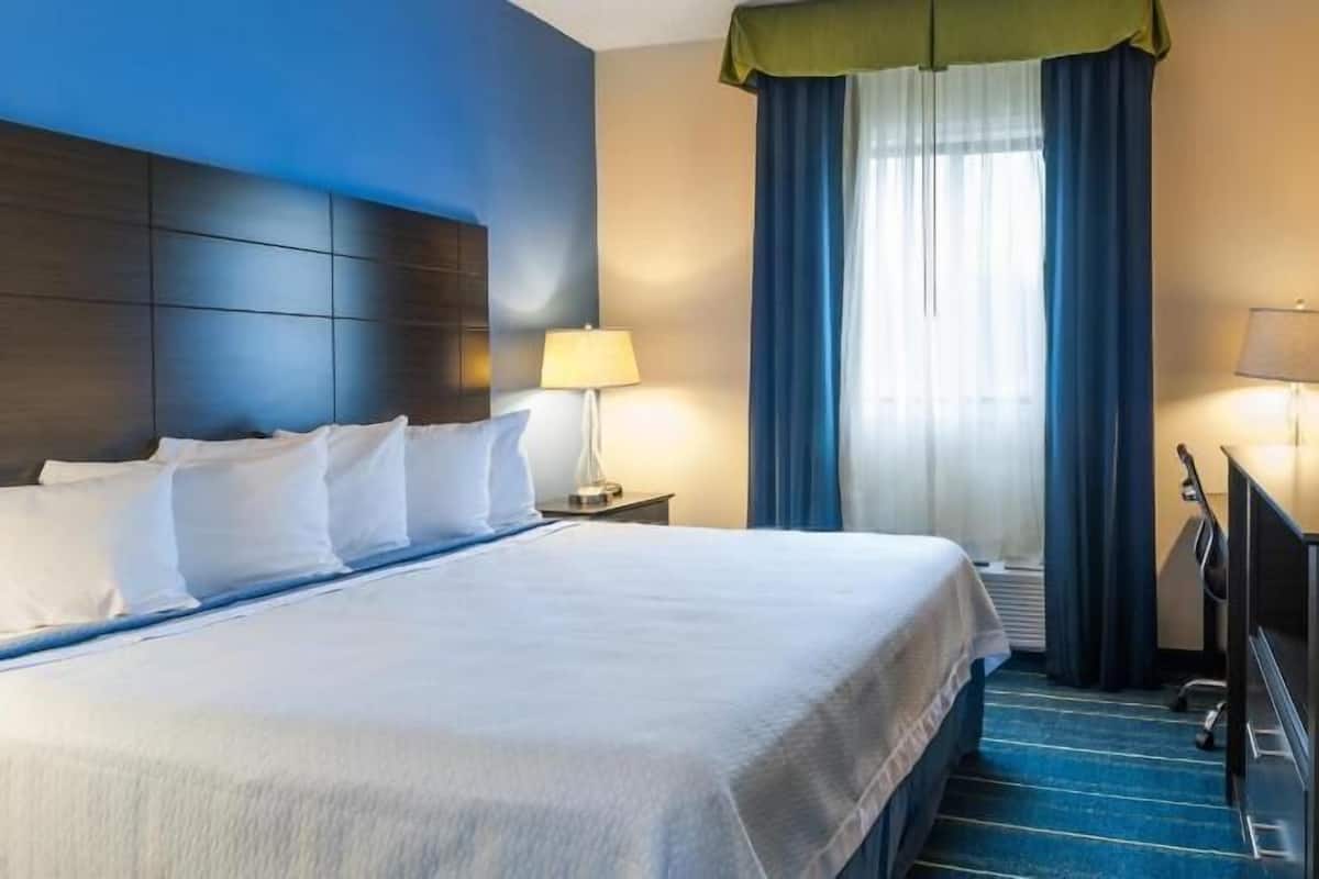 A hotel room with a large bed, two bedside tables with lamps, a desk with a chair, and a television on the wall.