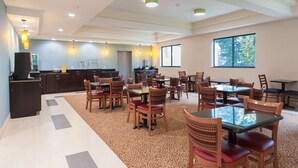 A spacious dining area with multiple tables and chairs, a kitchen in the background, and large windows allowing natural light. - Days Inn by Wyndham Tamworth (Chocorua)