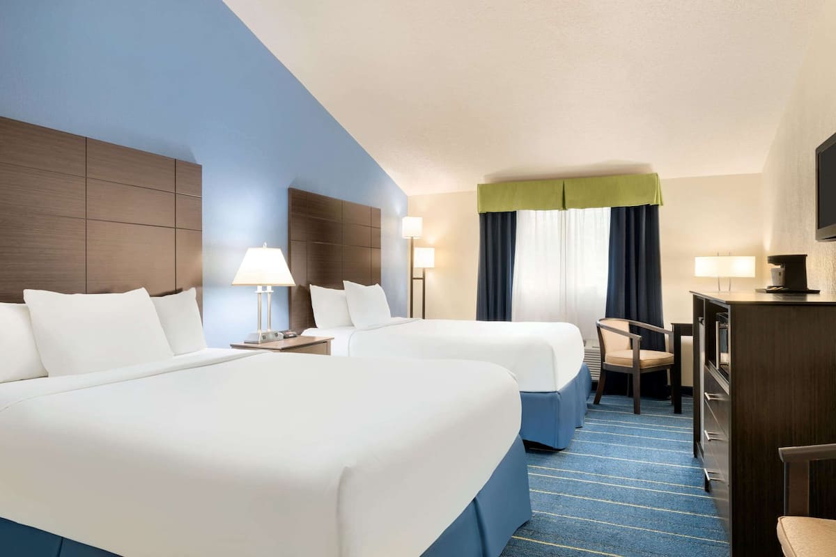 A hotel room with two beds, a desk, a chair, and a TV.