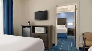 A hotel room with a large bed, a desk with a microwave, a television, and a chair.