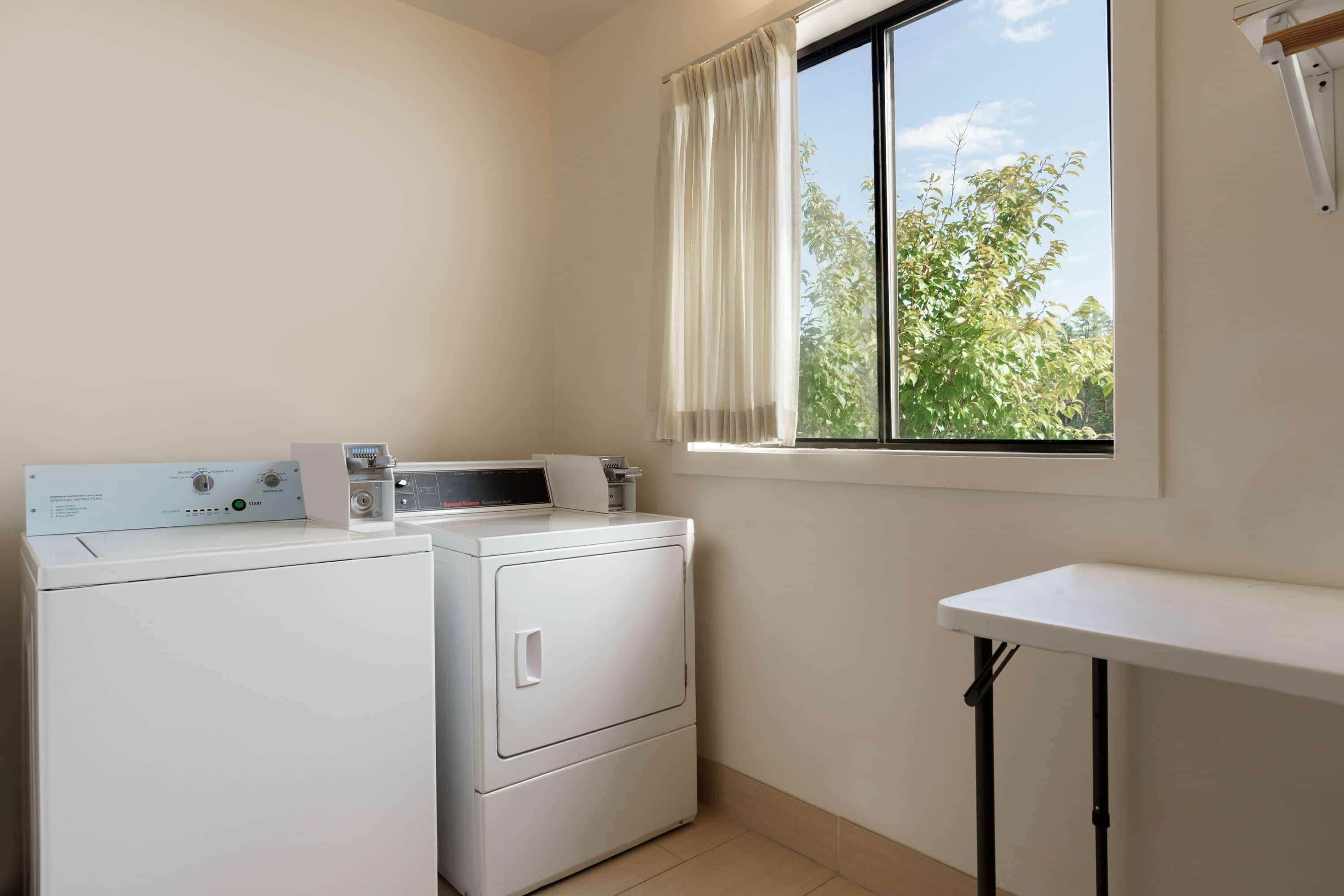 A laundry area with a washing machine and dryer, a small table, and a window with curtains.