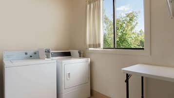 A laundry area with a washing machine and dryer, a small table, and a window with curtains.