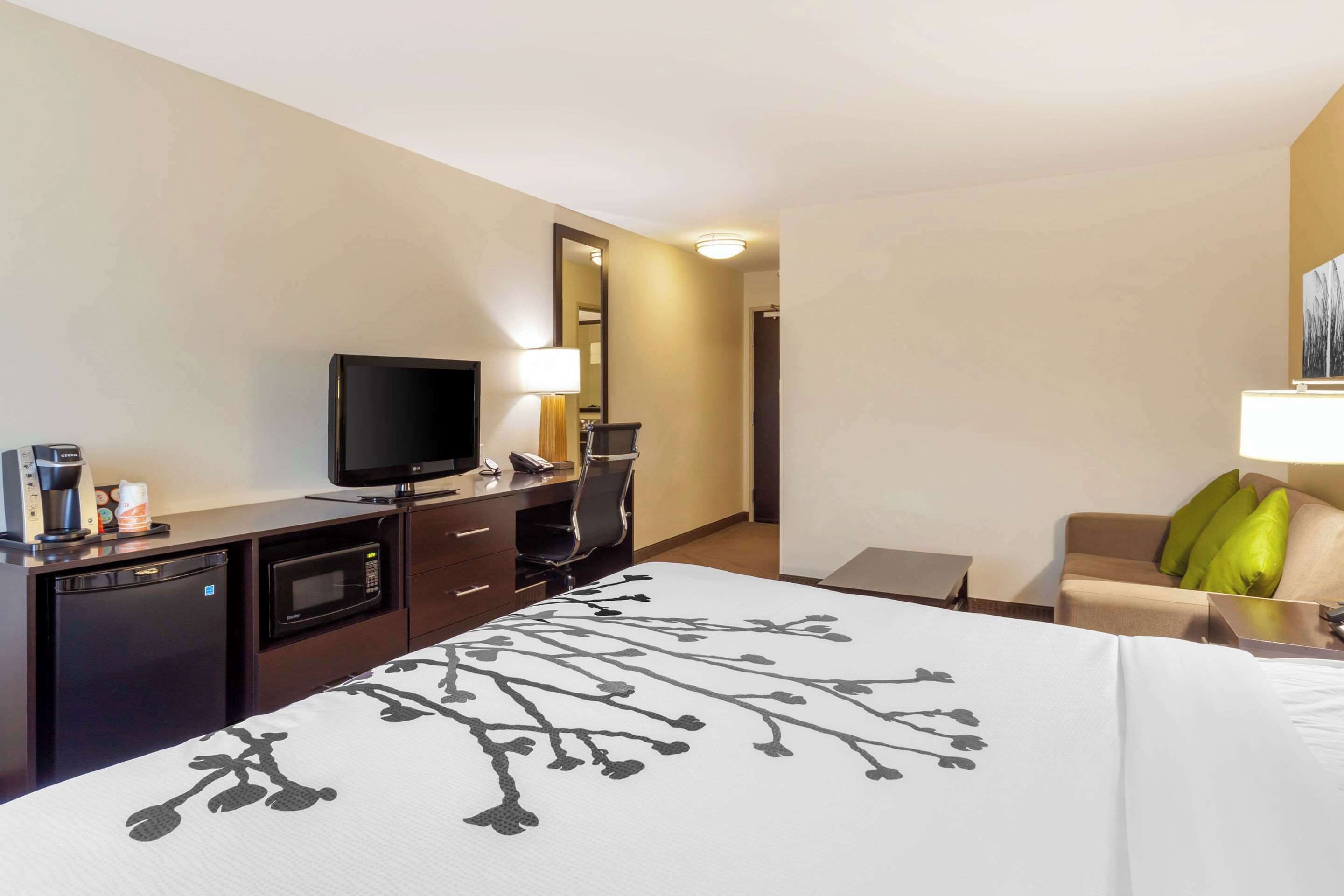 Una habitación de hotel con una cama, un escritorio con televisor, un microondas y una cafetera.