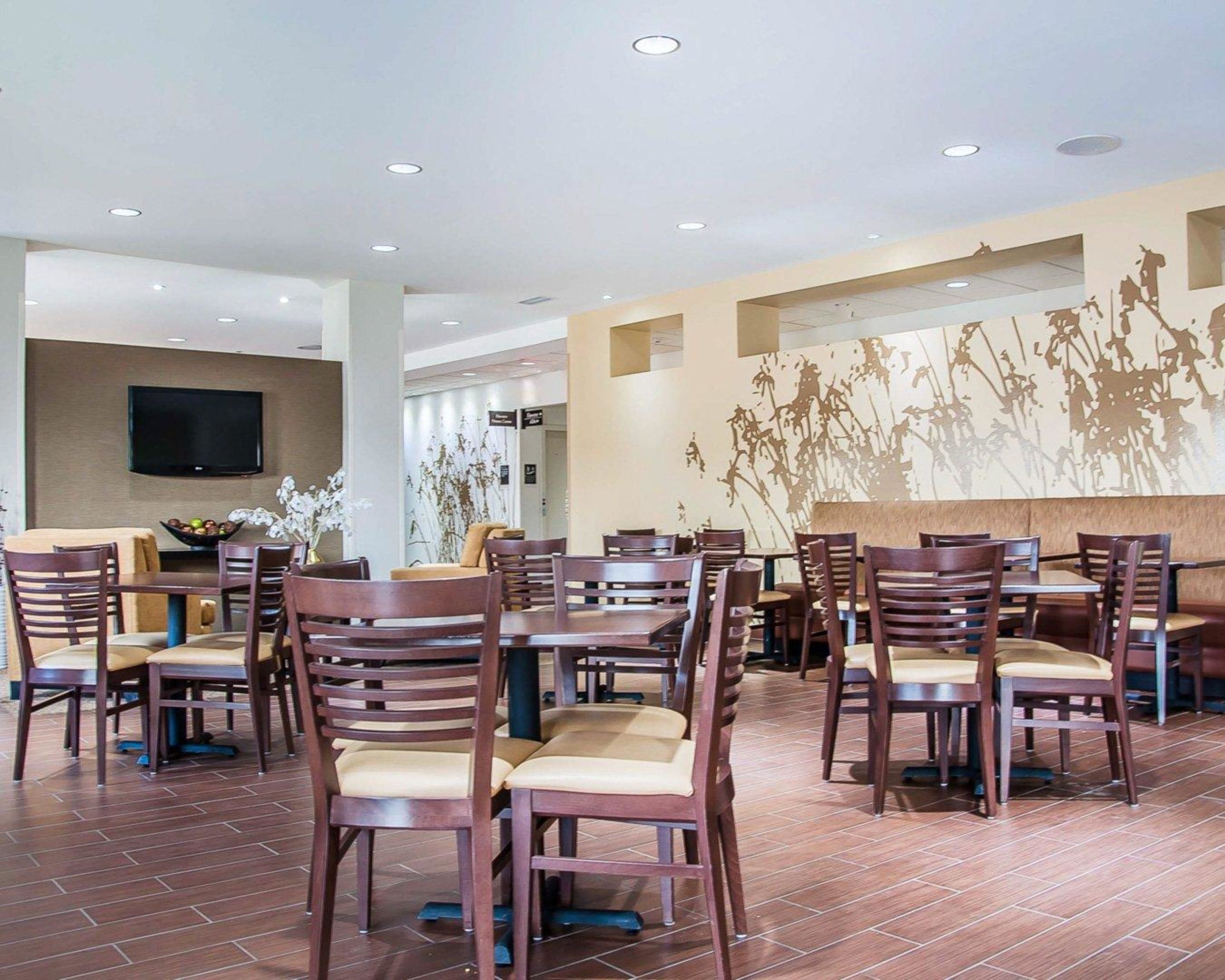 A spacious dining area with multiple tables and chairs, a flat-screen TV mounted on the wall, and a decorative wall mural.