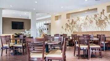 A spacious dining area with multiple tables and chairs, a flat-screen TV mounted on the wall, and a decorative wall mural.