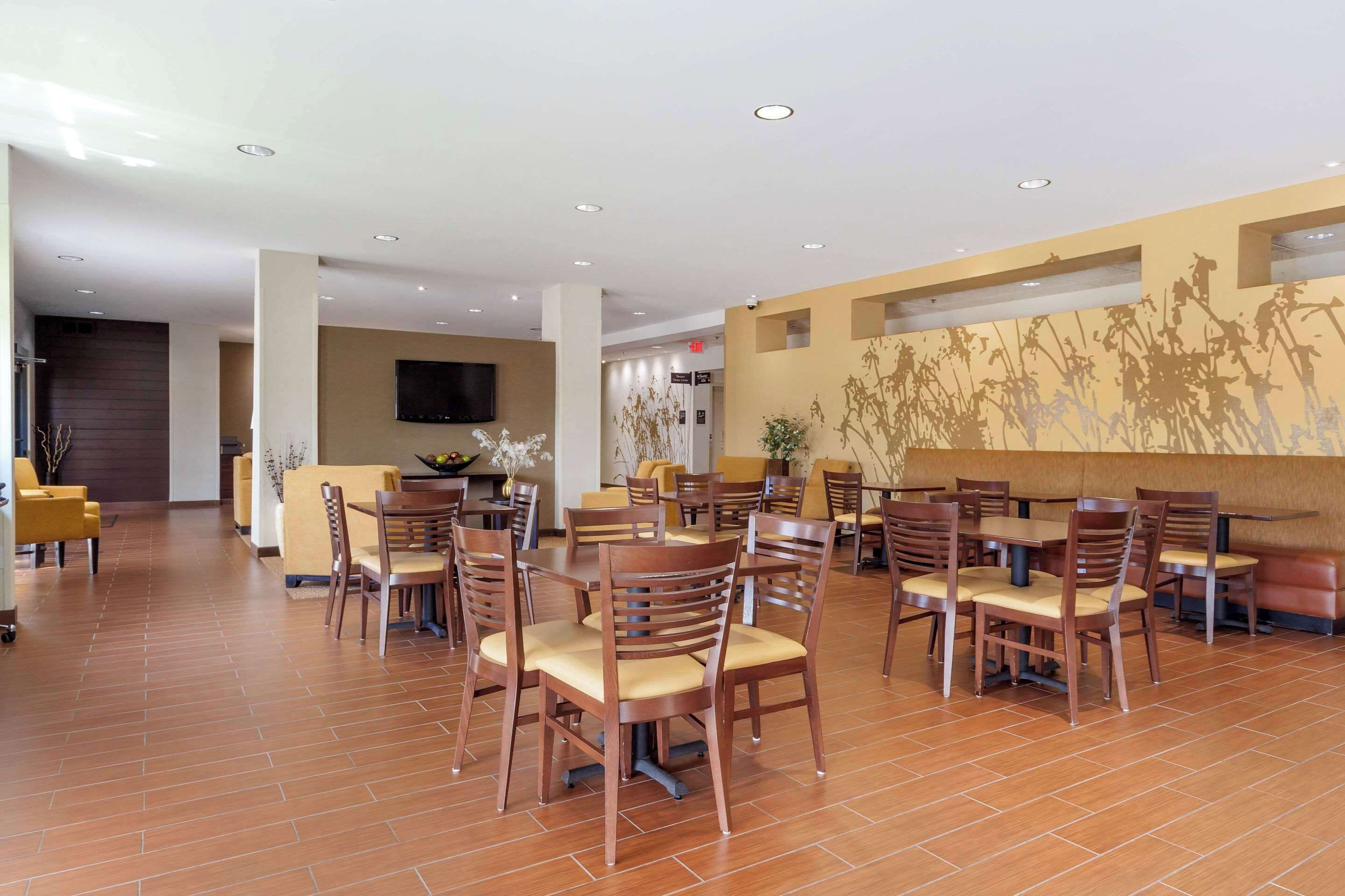 A spacious dining area with multiple wooden tables and chairs, a flat-screen TV mounted on the wall, and a decorative wall mural.
