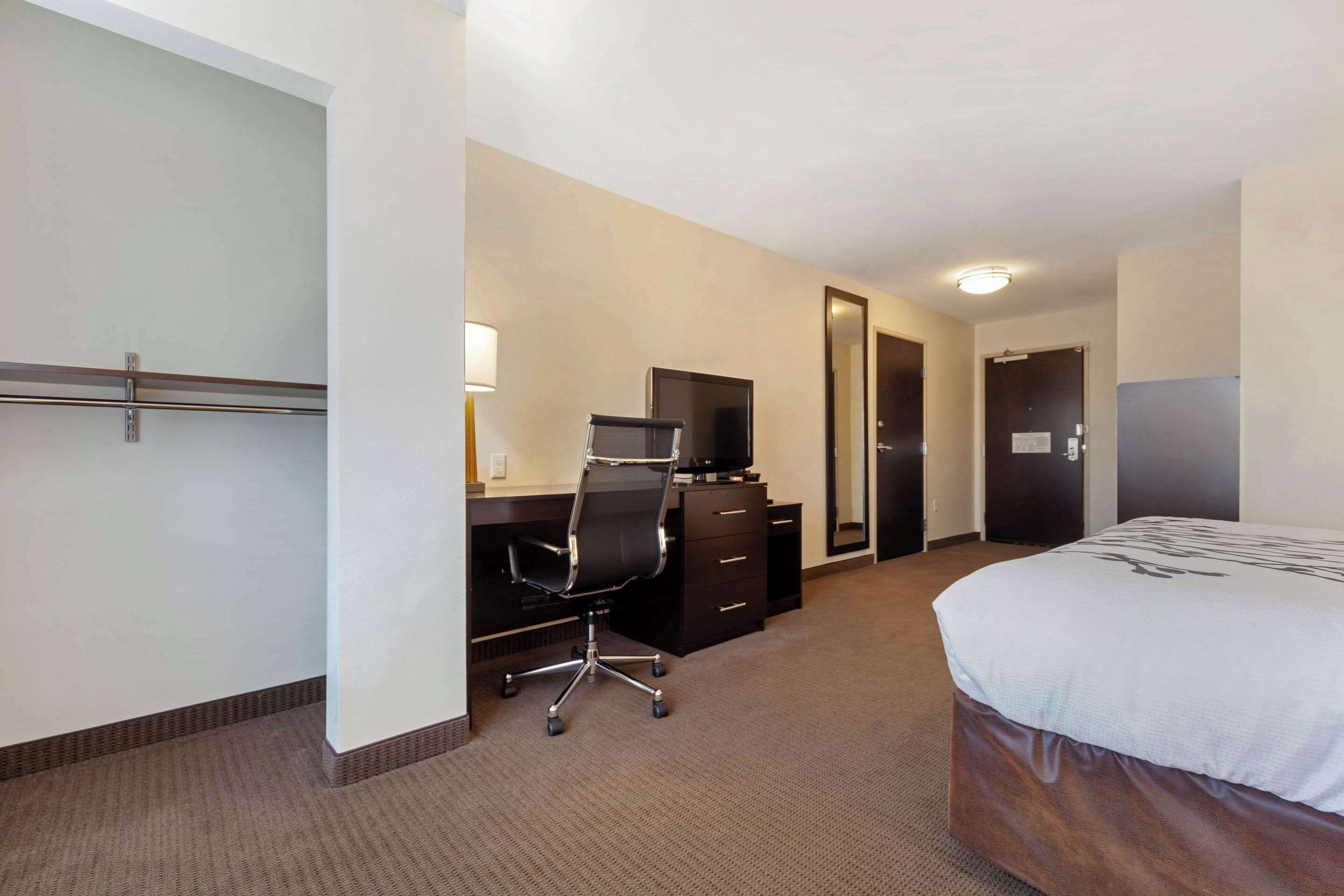 A hotel room with a bed, a desk with a chair, a television, and a wardrobe.