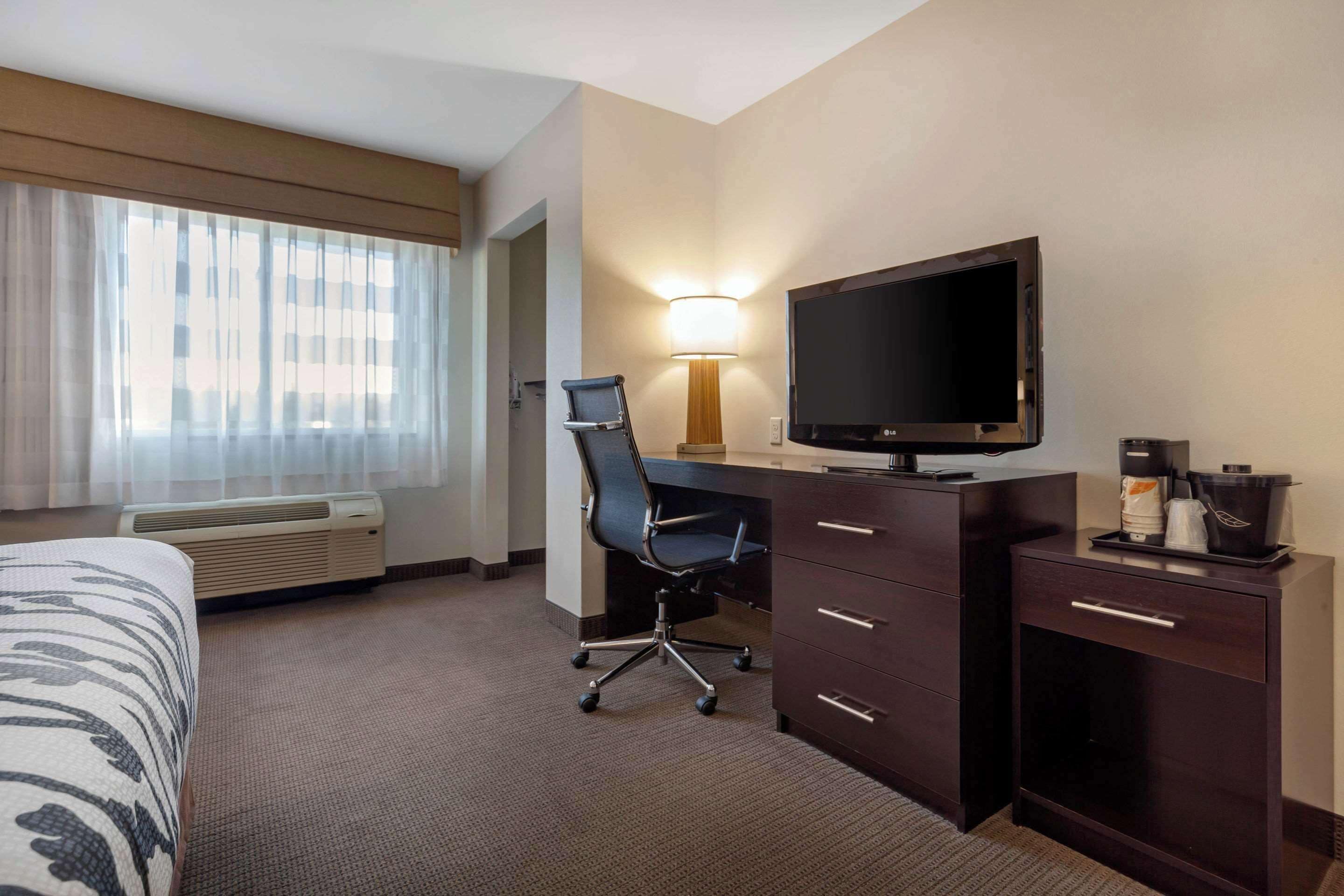 Une chambre d’hôtel équipée d’un lit, d’un bureau avec un ordinateur, d’une télévision, d’une chaise, d’une lampe et d’une machine à café.