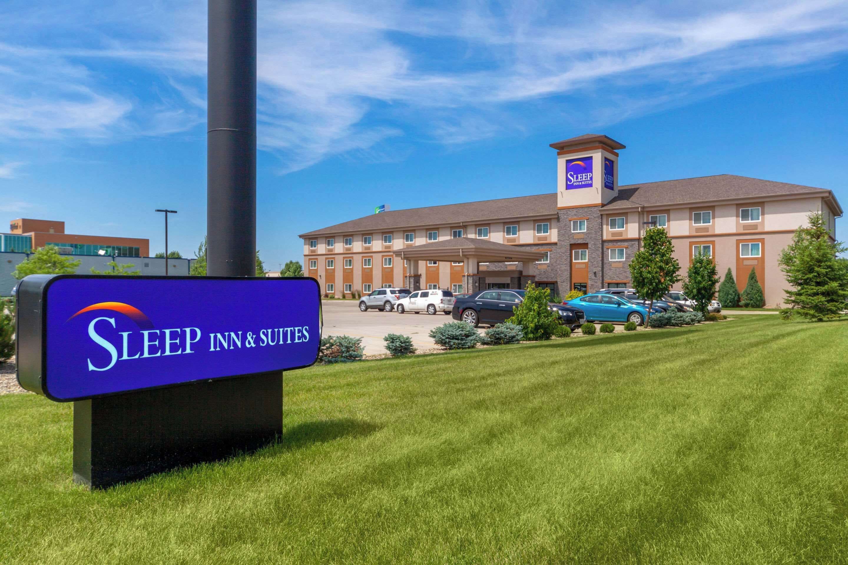 A Sleep Inn & Suites building with a parking lot and a grassy area in front.