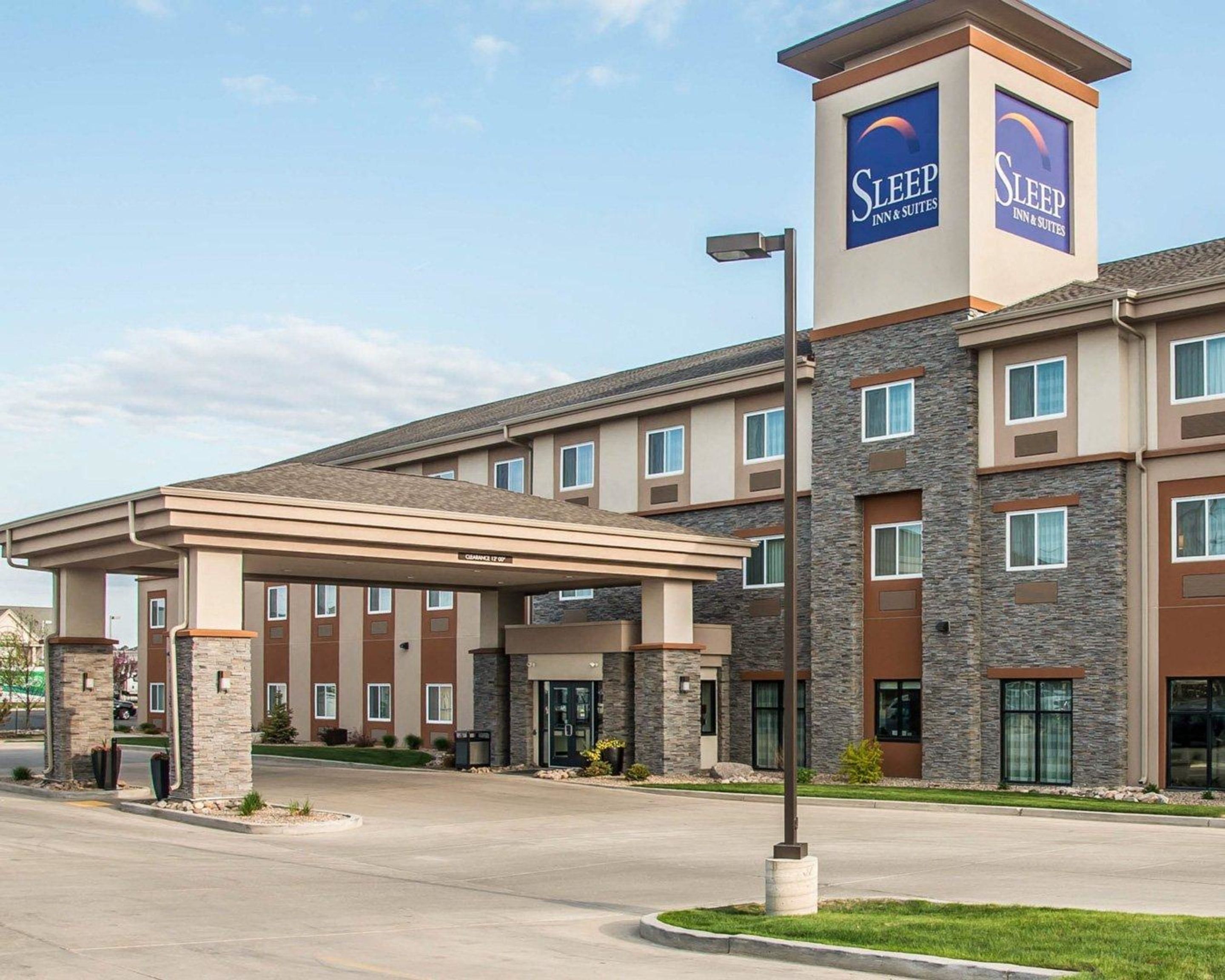 A Sleep Inn & Suites hotel with a covered entrance, multiple floors, and a prominent tower with the hotel's logo.