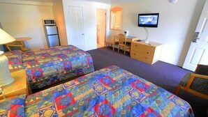 Ett hotellrum med två sängar, ett skrivbord, en stol, en tv och ett kylskåp.