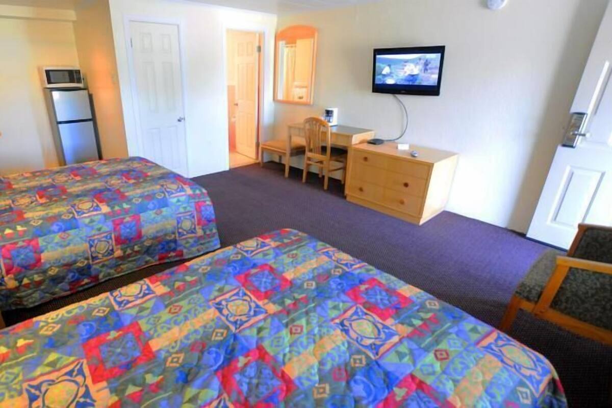 A hotel room with two beds, a desk, a chair, a television, and a refrigerator.