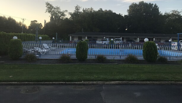 Ett hotell med en swimmingpool, en inhägnad parkeringsplats och en byggnad med ett platt tak.