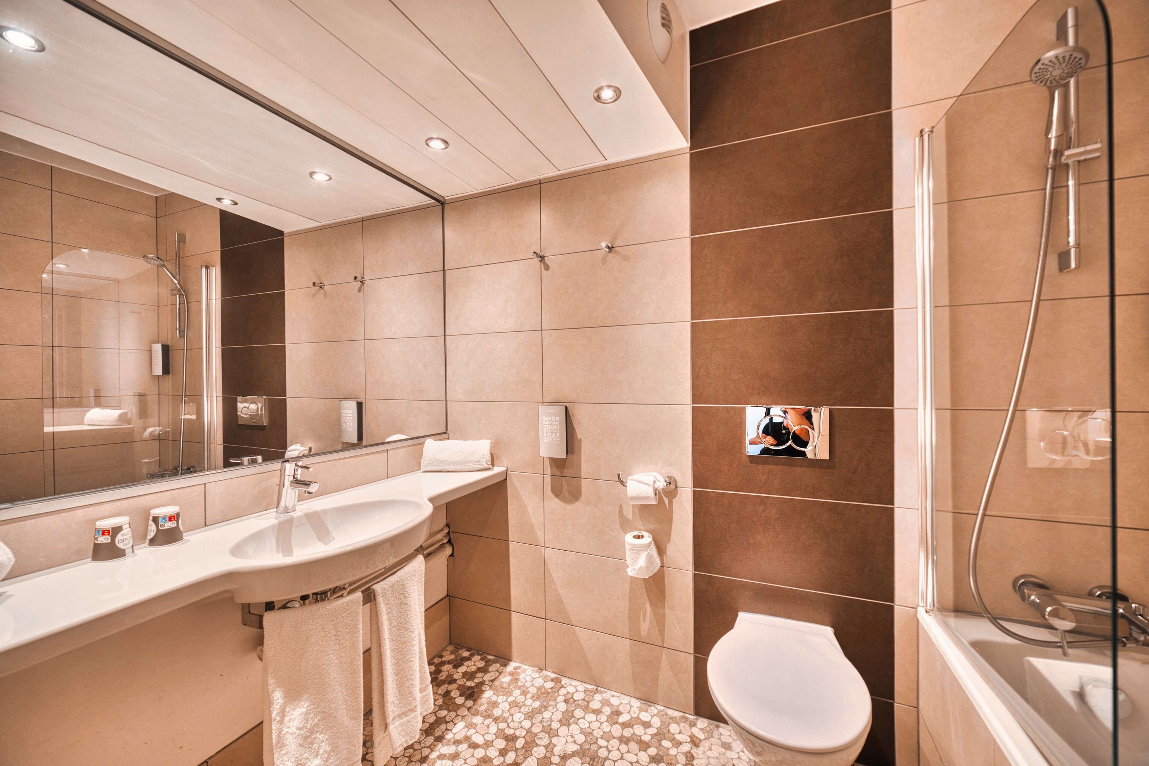 A modern bathroom with a large mirror, a sink, a toilet, and a shower.