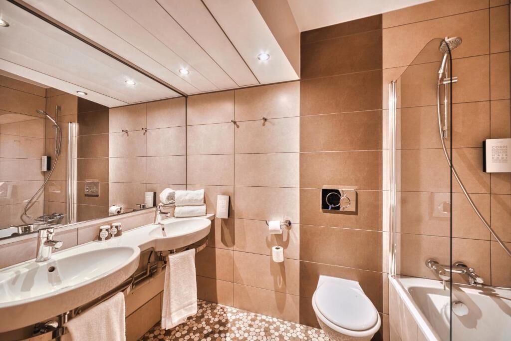 Une salle de bain moderne avec un grand miroir, deux lavabos, des toilettes et une baignoire.