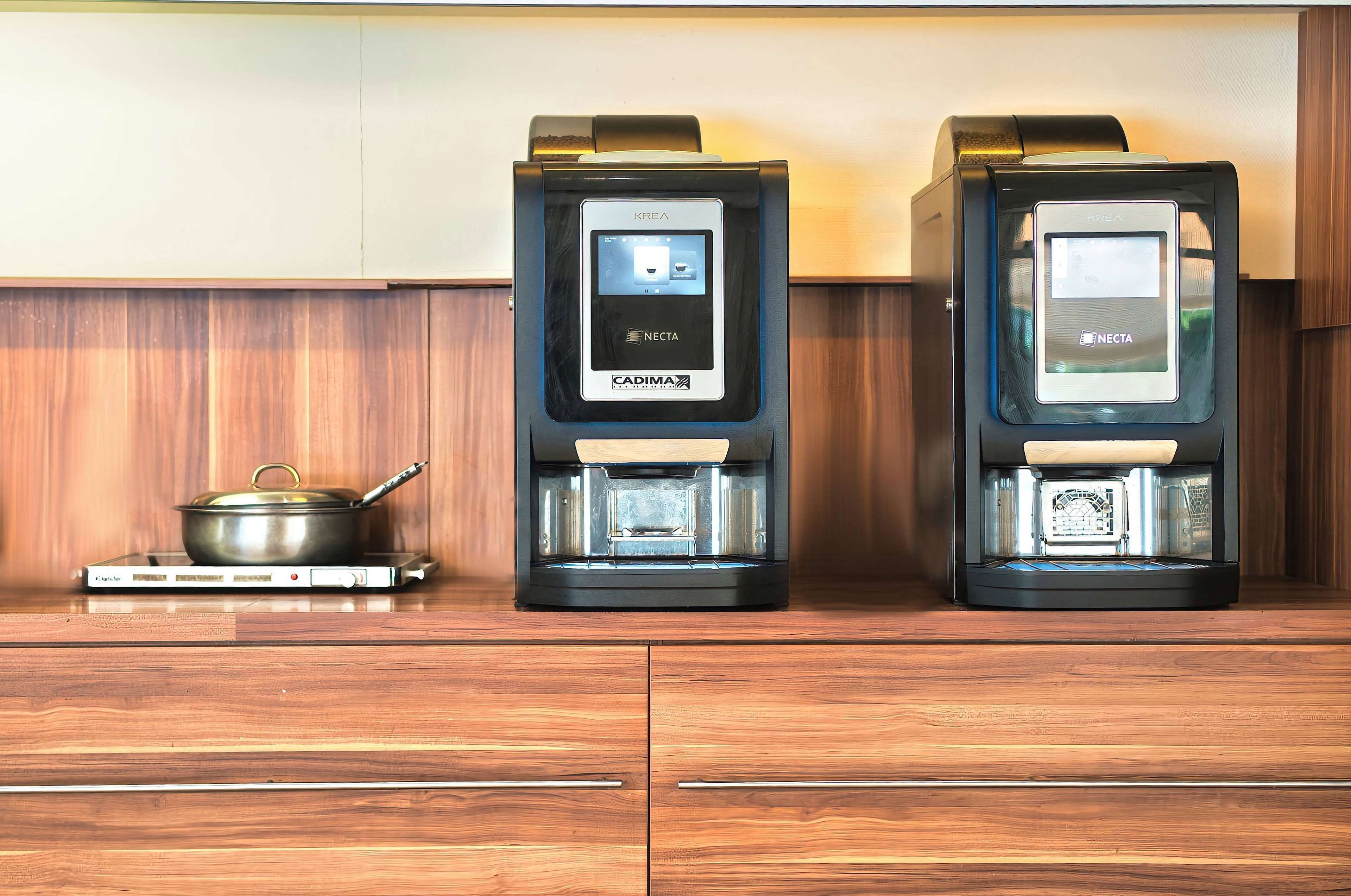 Dos cafeteras con interfaces digitales y una olla sobre una hornilla portátil.