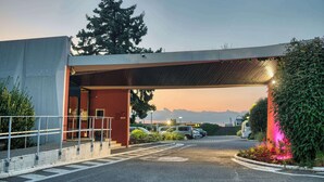 A parking area with cars, a covered walkway, and a building entrance. - KYRIAD PRESTIGE MULHOUSE - Basel (Sausheim)