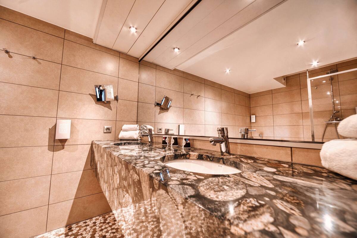 Une salle de bain moderne avec un grand lavabo, un comptoir en marbre et un grand miroir.