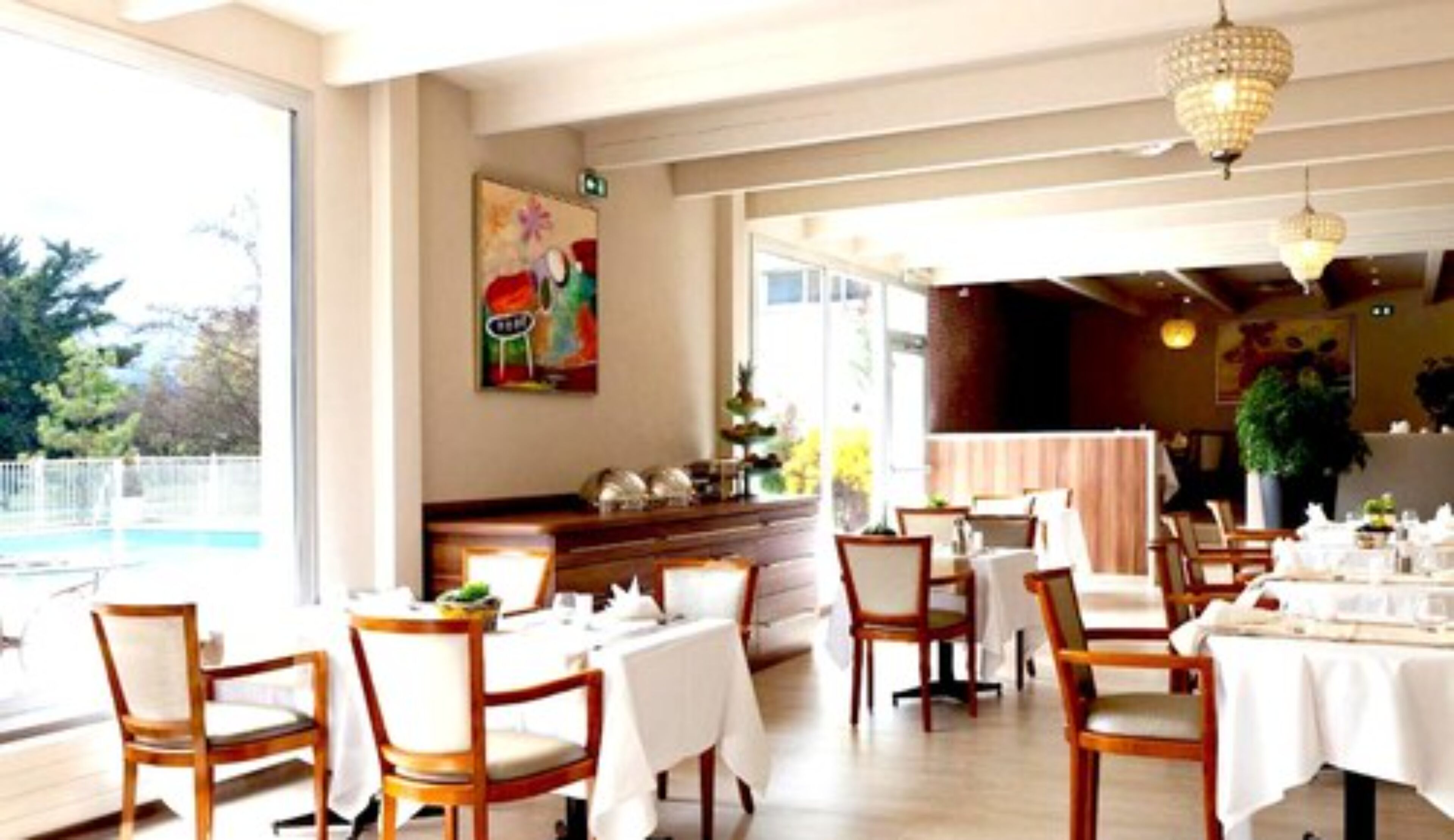 A dining area with tables set for two, wooden chairs, and a chandelier.