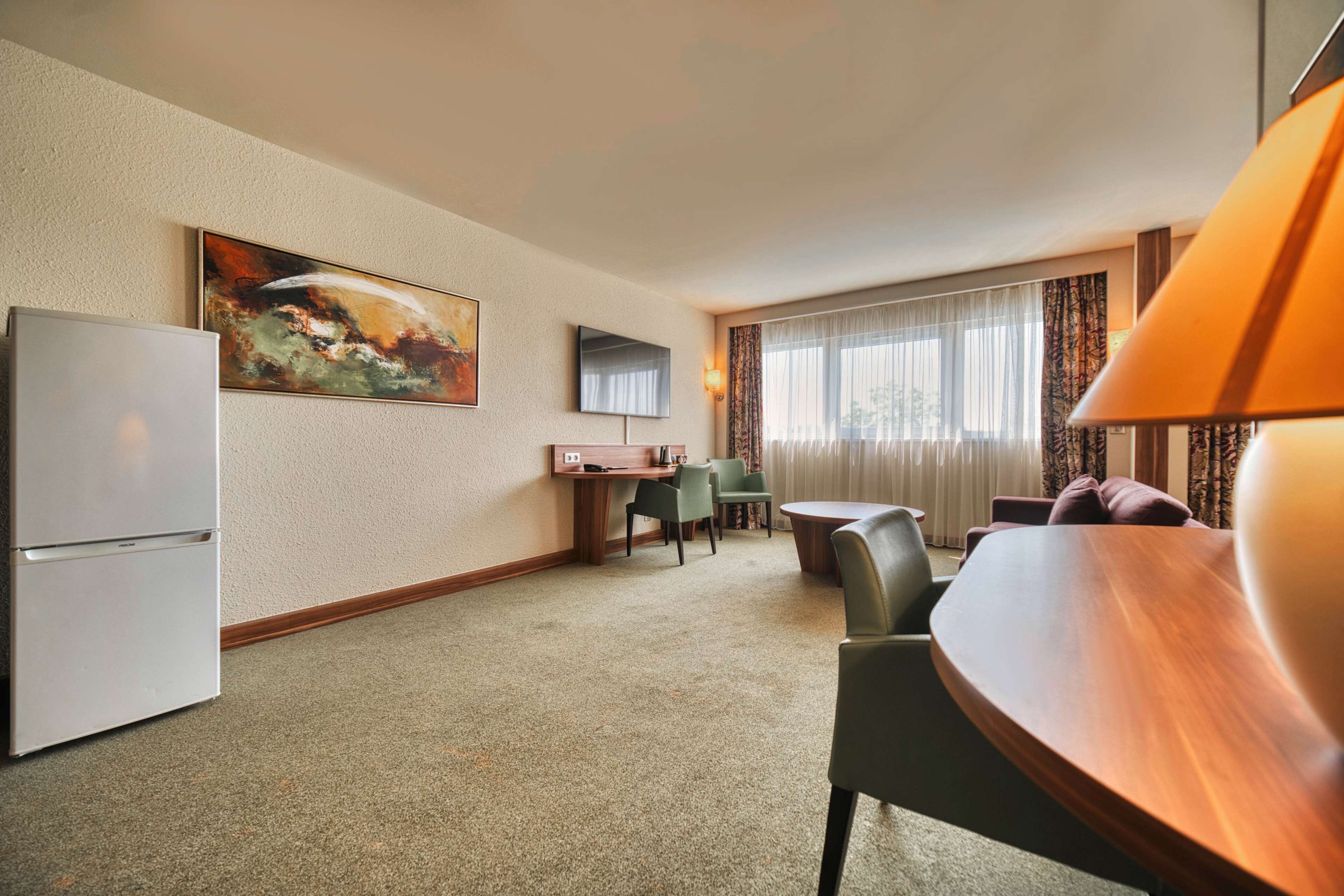 Une chambre d’hôtel comprenant un coin repas, un réfrigérateur, un tableau, une télévision et une lampe.