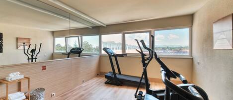 A gym with exercise equipment, a wooden floor, a window with a view, and a mirror on the wall.