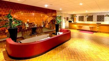 A reception area with a curved red counter, a stone wall with plants, and a herringbone floor pattern.