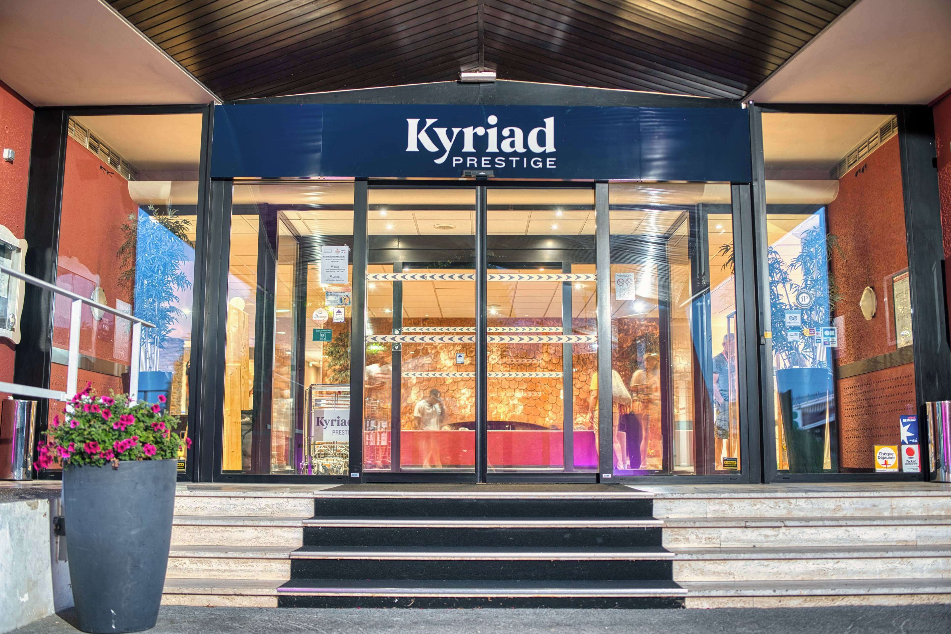 L'ingresso del Kyriad Prestige con porte in vetro, interni ben visibili e gradini che conducono all'accesso.
