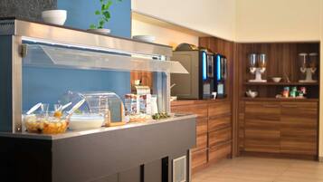 Zona de buffet con un recinto de vidrio, diversos alimentos y electrodomésticos de cocina al fondo.