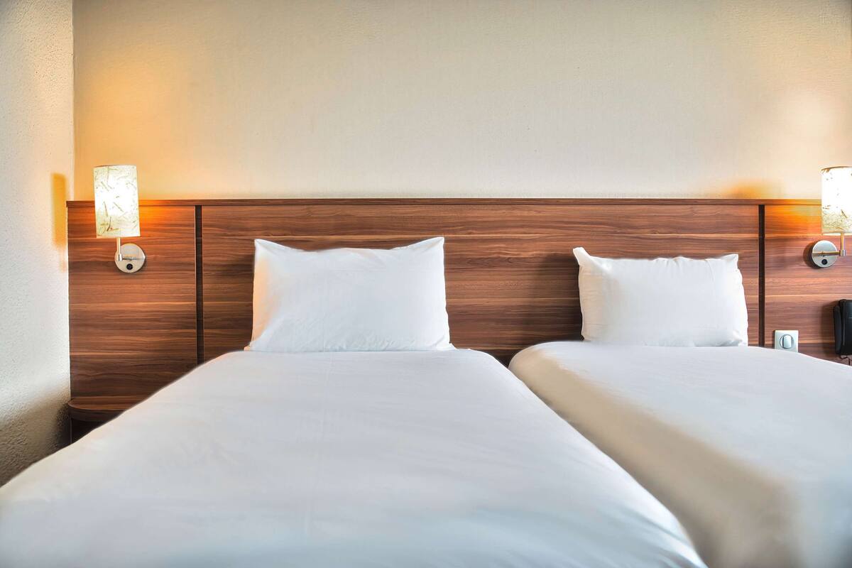 Une chambre d’hôtel avec deux lits, une tête de lit en bois et des lampes fixées au mur.