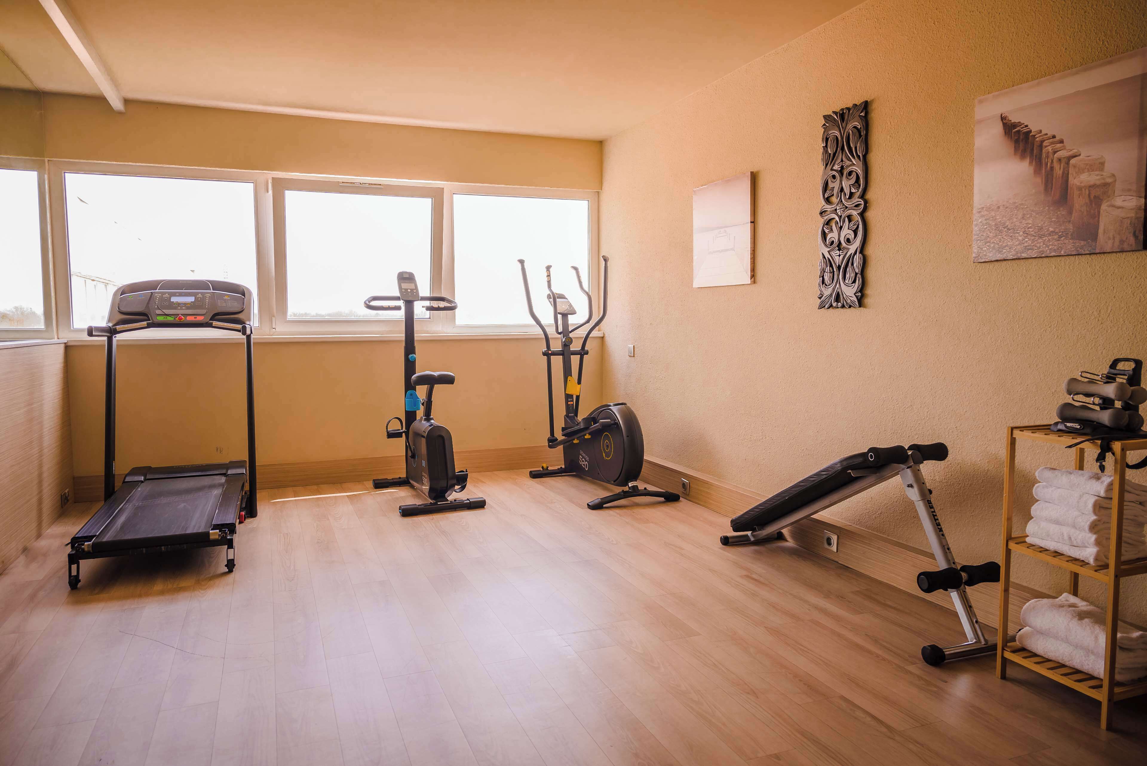Et fitnessrum med løbebånd, crosstrainer, motionscykel og bænk.