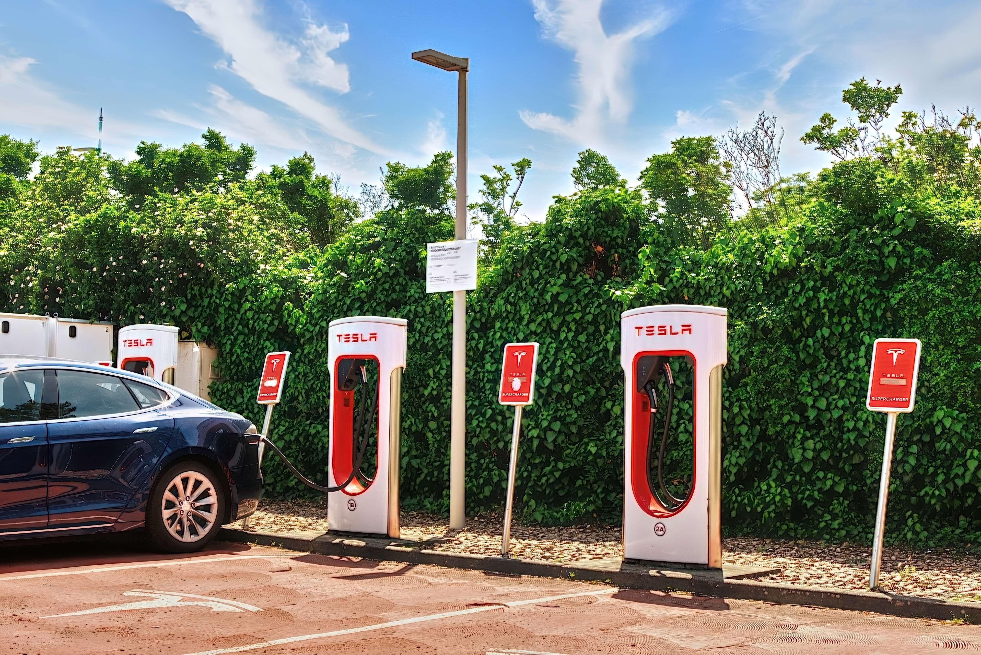 Una estación de carga de Tesla con un coche azul estacionado cerca.