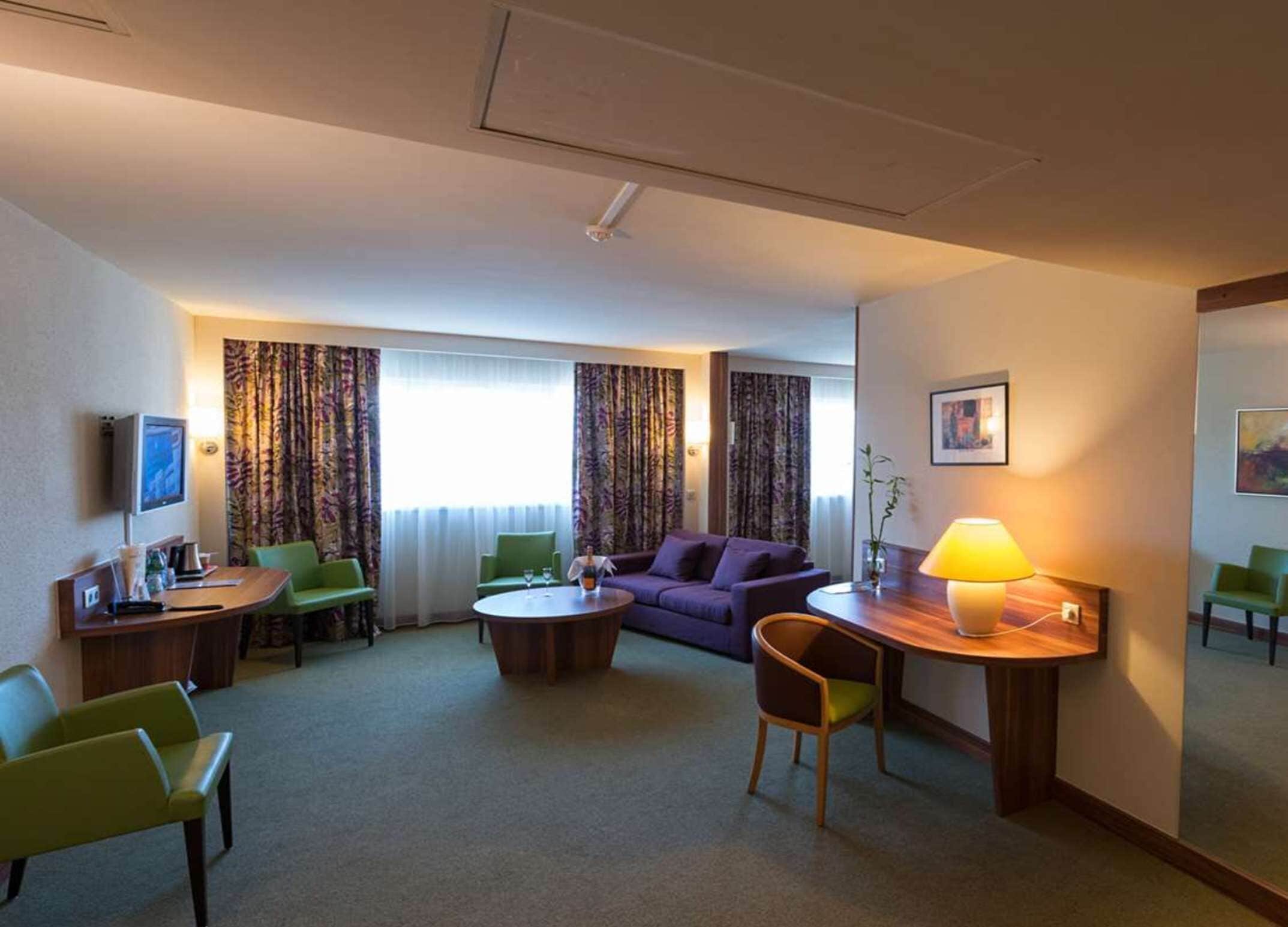 A hotel room with a sofa, two armchairs, a coffee table, a TV, and a lamp.