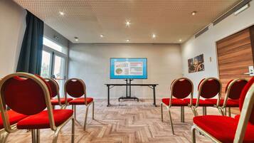 A conference room with red chairs, a presentation screen, and a herringbone-patterned floor.