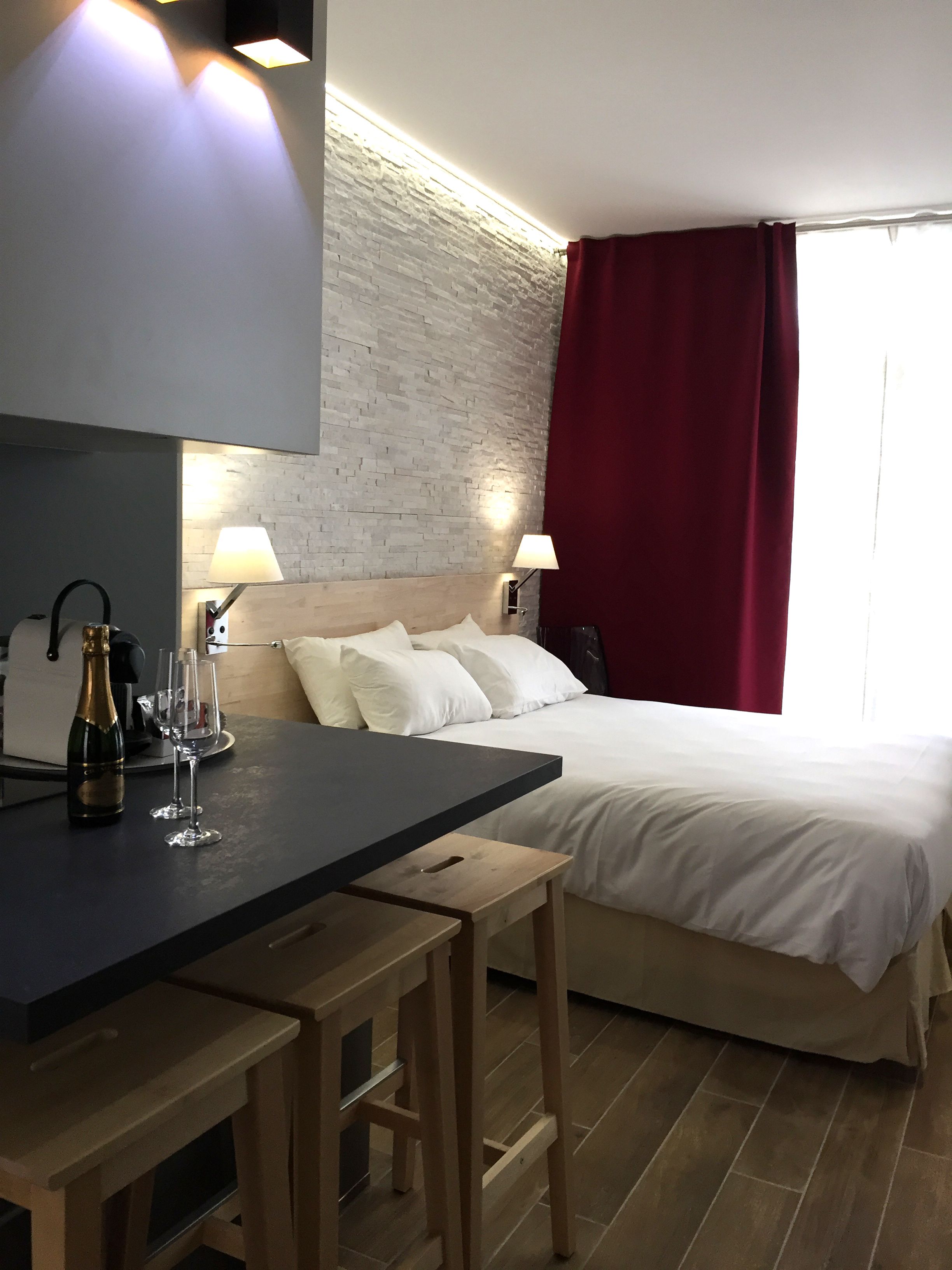 Ein Hotelzimmer mit einem Bett, Nachttischlampen, einem Holztisch mit einer Flasche und Gläsern sowie einer Wand mit Backsteinmuster.